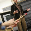 Woman in blazer standing in background, hands holding percussion mallets in foreground
