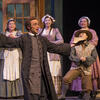 Three women and two men on stage in peasant costumes, male singer in foreground with arms open singing. 