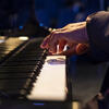 Keyboard of a grand piano with hands hovering over it. 