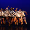 Seven dancers all leaning to one side with same arm in curved upward