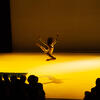 Dancer onstage jumping in air with arms above their head 